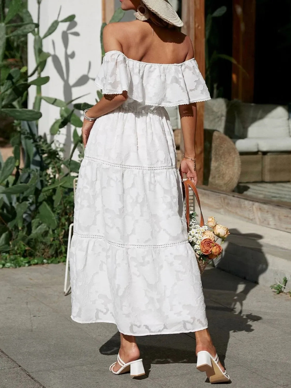 Back view of a white off-shoulder tiered maxi dress, showcasing the elastic waist and flowing skirt with lace trim details.