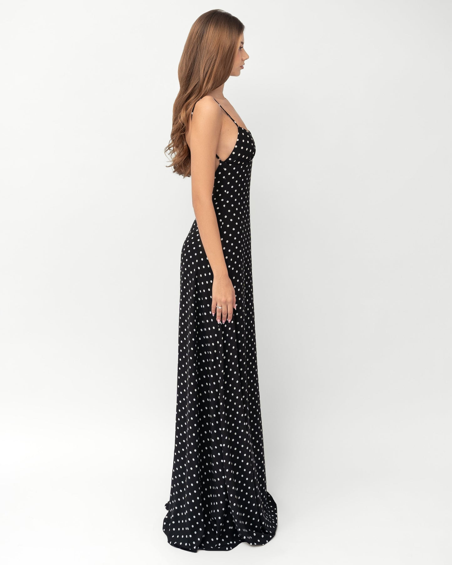 Side profile of black polka dot maxi dress showing slim fit, spaghetti straps, and floor length hem
