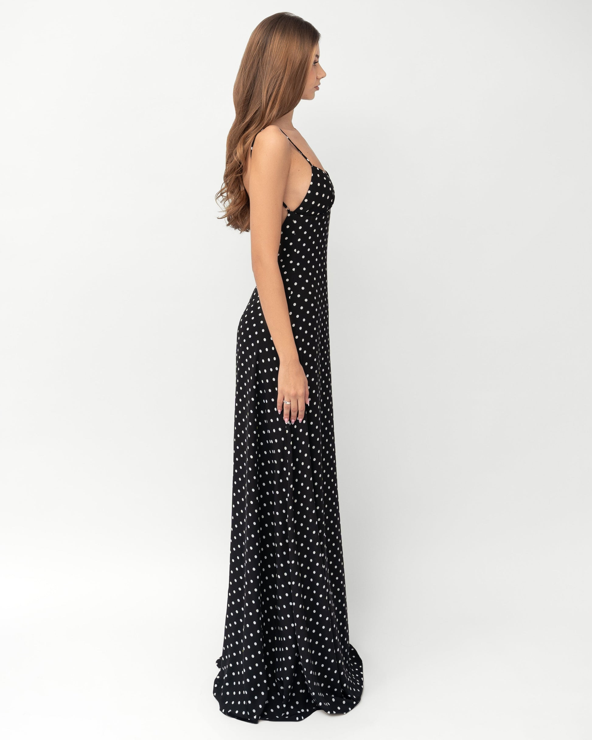 Side profile of black polka dot maxi dress showing slim fit, spaghetti straps, and floor length hem