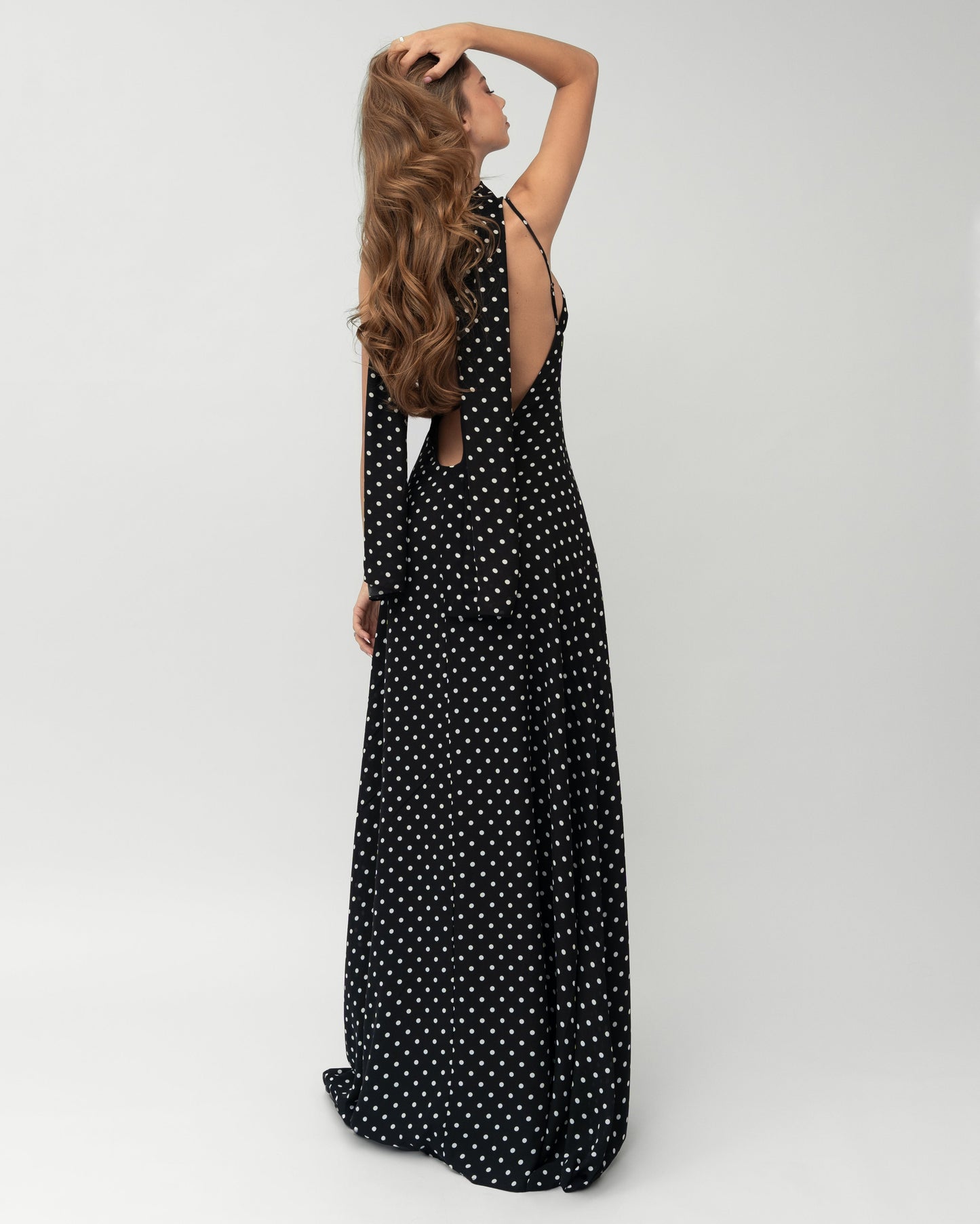 Back angled view showing dramatic open back on black polka dot maxi dress with scarf drape