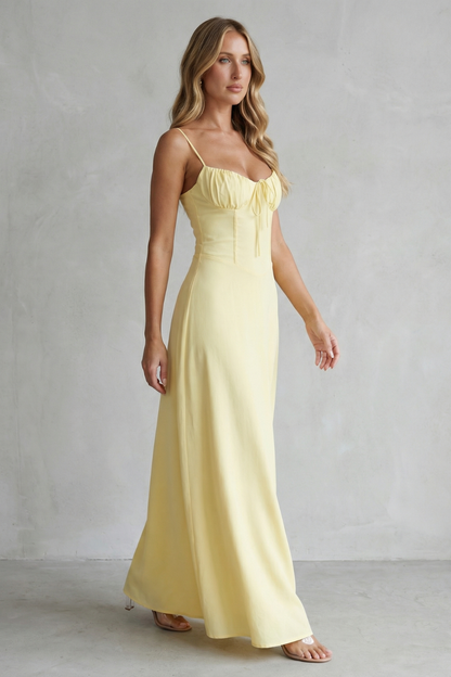 Side profile of a women's yellow maxi dress with a flowing skirt, sweetheart neckline, and thin straps, ideal for vacation outfits.