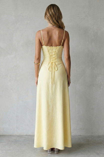 Back view of a women's yellow maxi dress showcasing a lace-up corset detail on the back, a unique design for wedding guest dresses.
