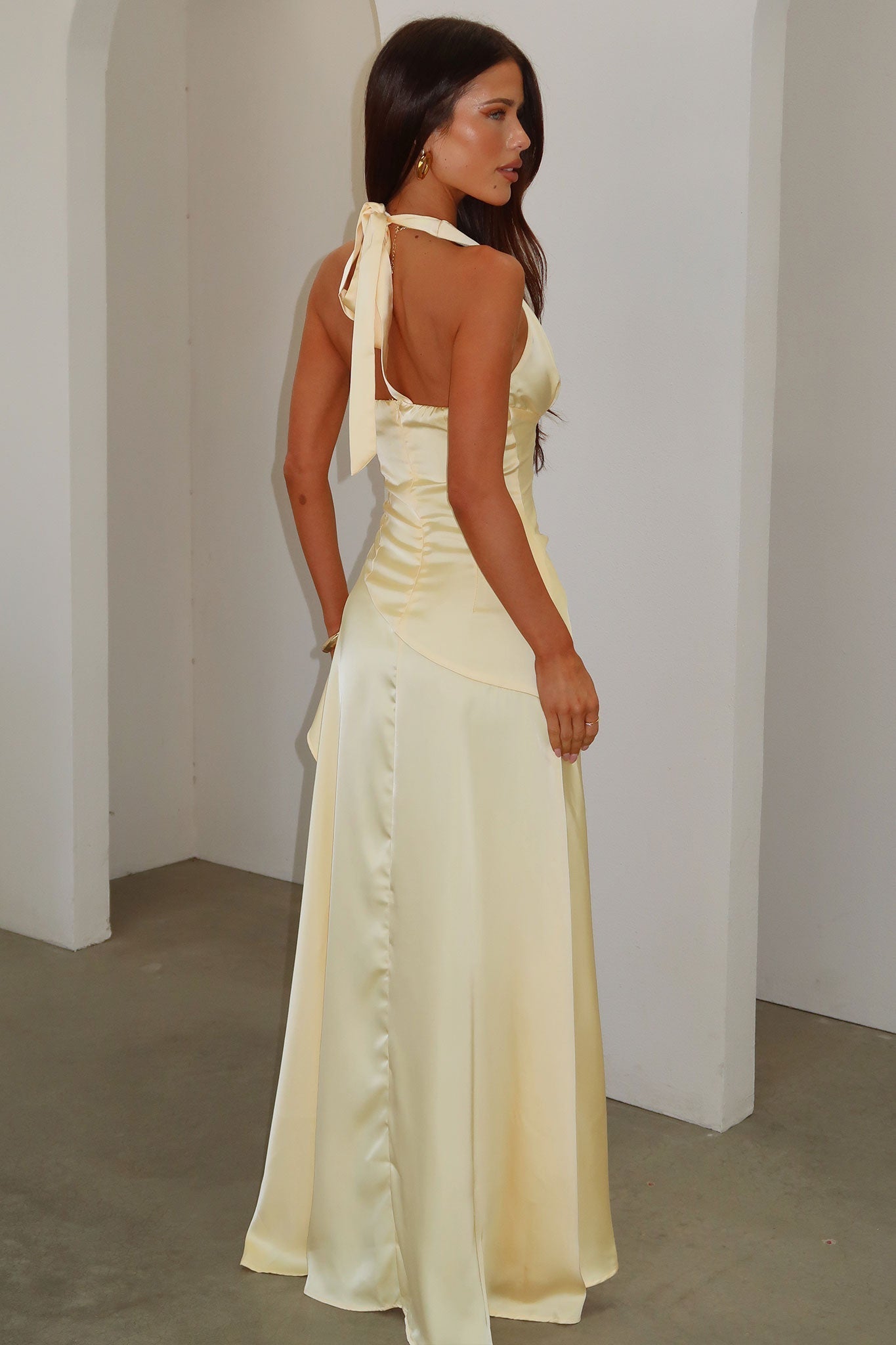 Side back view of pale yellow satin maxi dress with open back, neck tie and fitted corset waist