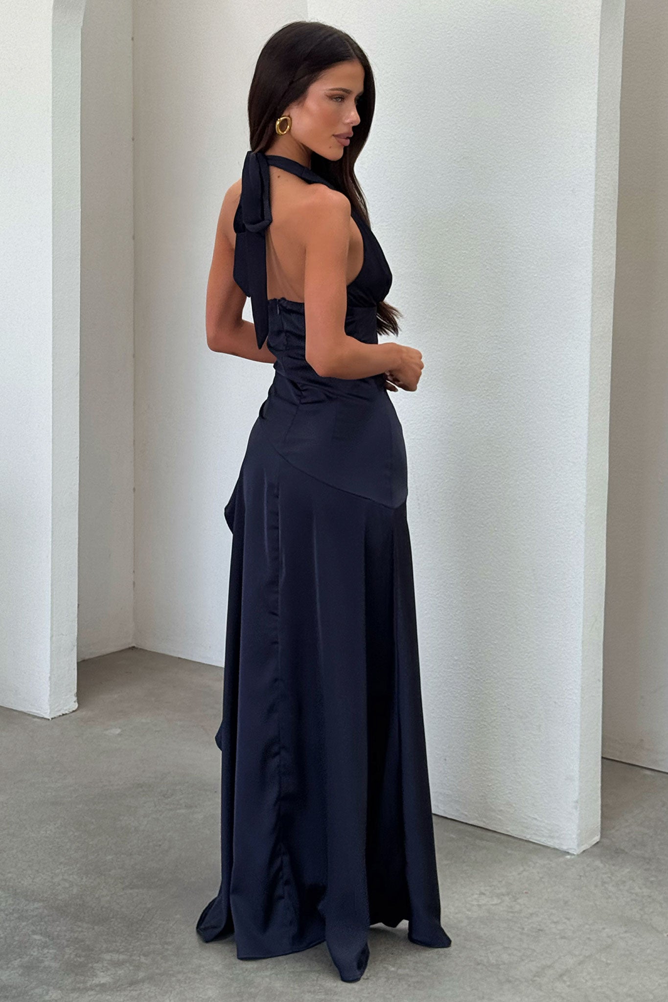 Back three-quarter view of navy satin maxi dress with halter neck bow and fitted corset waist