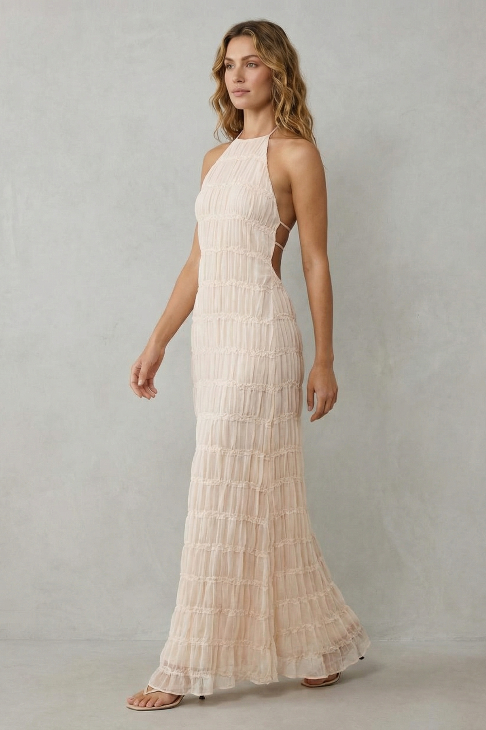 Side view of the light pink textured halter open back maxi dress, highlighting the fitted bodice and flowing skirt.