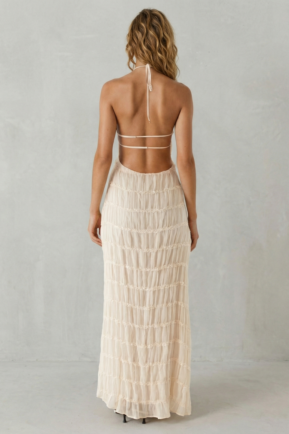 Back view of the light pink textured halter open back maxi dress, showing the delicate strap details.