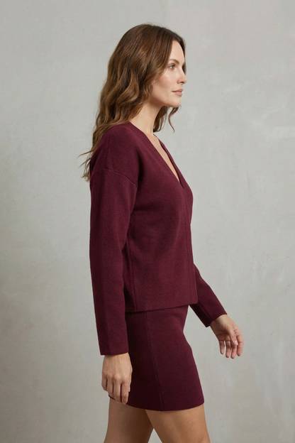 Side profile of a women's maroon knit long sleeve v-neck top and coordinating mini skirt set.
