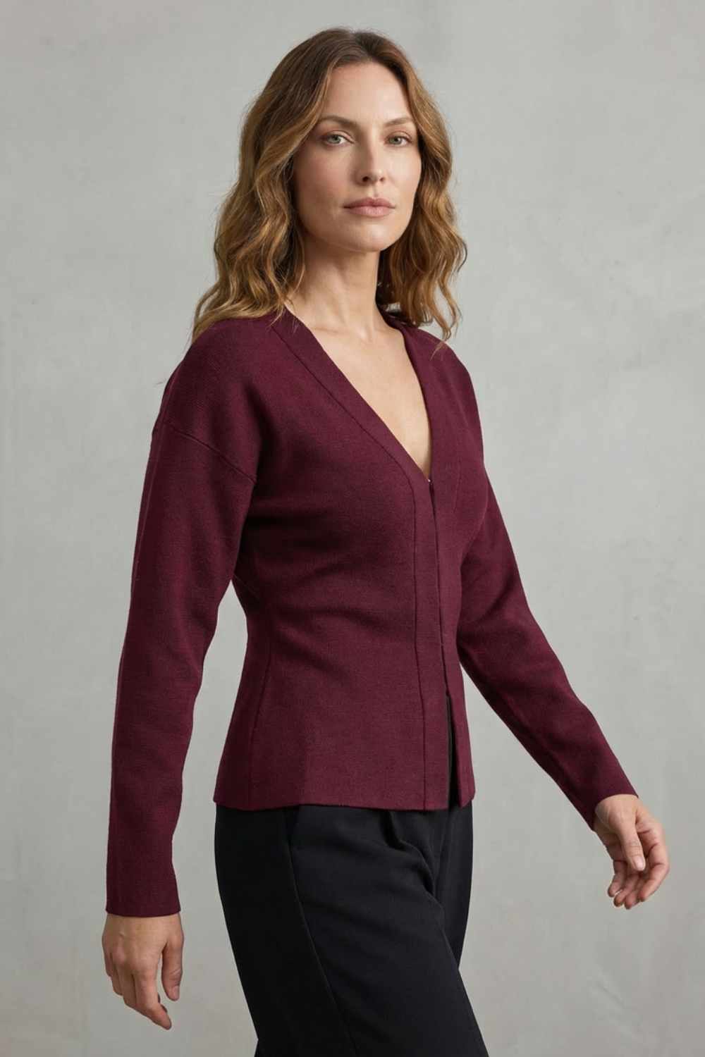 Side profile of a women's maroon knit long sleeve v-neck top, styled with black pants.
