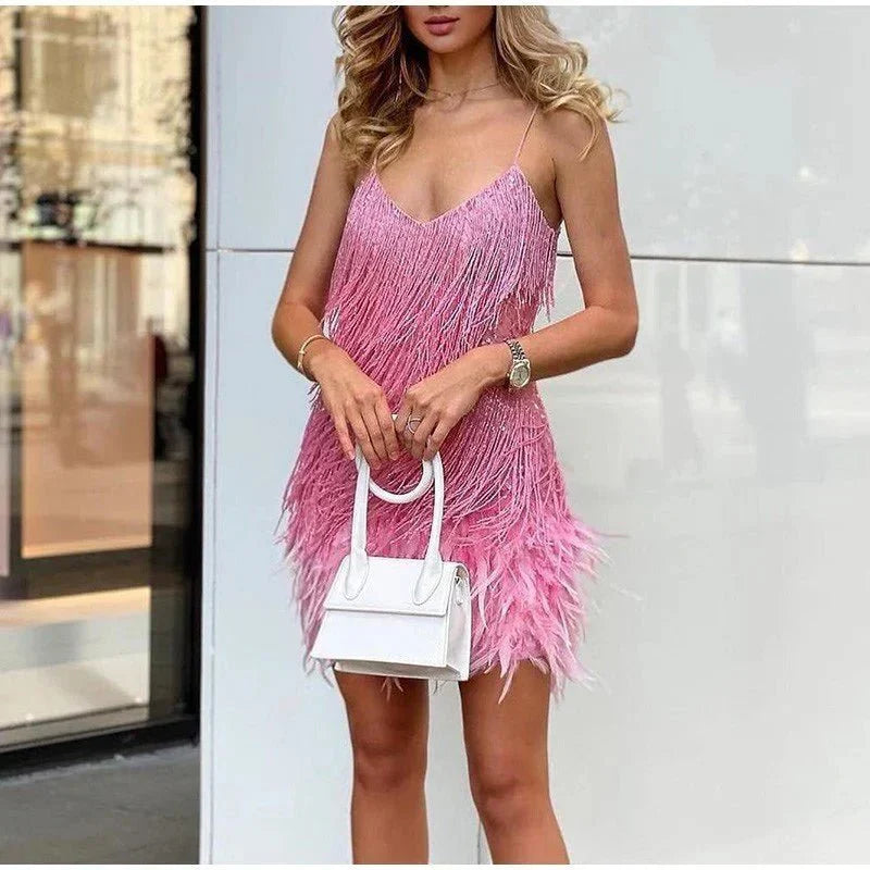 Pink V-neck sequin feather mini dress with a layered fringe effect, paired with a small white handbag.