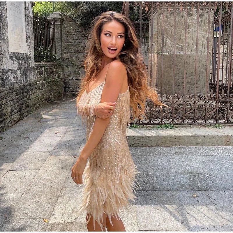 Champagne V-neck sequin feather mini dress with long flowing hair, looking over shoulder outdoors.