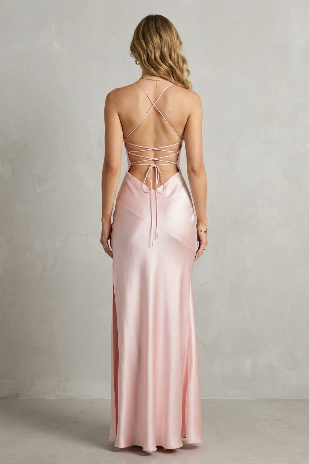 Back view of the light pink satin maxi dress, highlighting the criss-cross lace-up back detail and floor-length skirt.