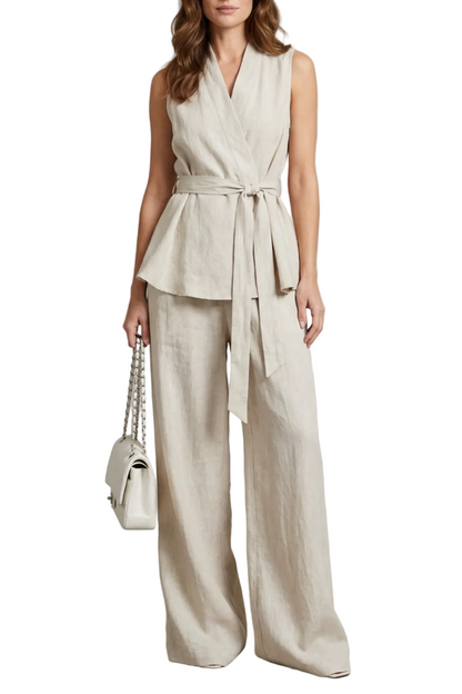 Full-length view of a woman wearing a beige linen V-neck sleeveless wrap top and wide leg pants set, holding a white quilted handbag.
