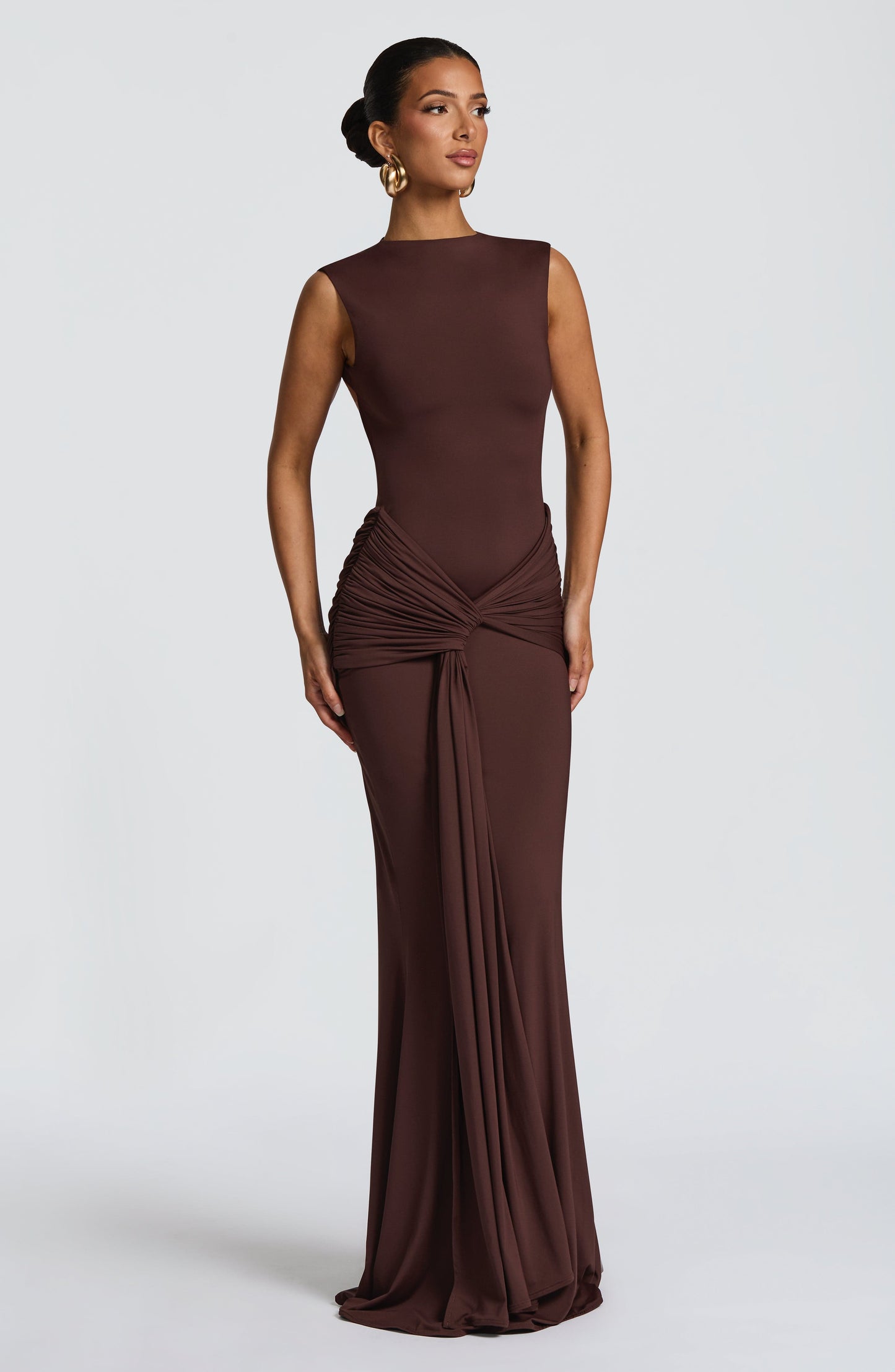 Chocolate brown wedding guest maxi dress in angled view, highlighting ruched hip wrap and drape detail