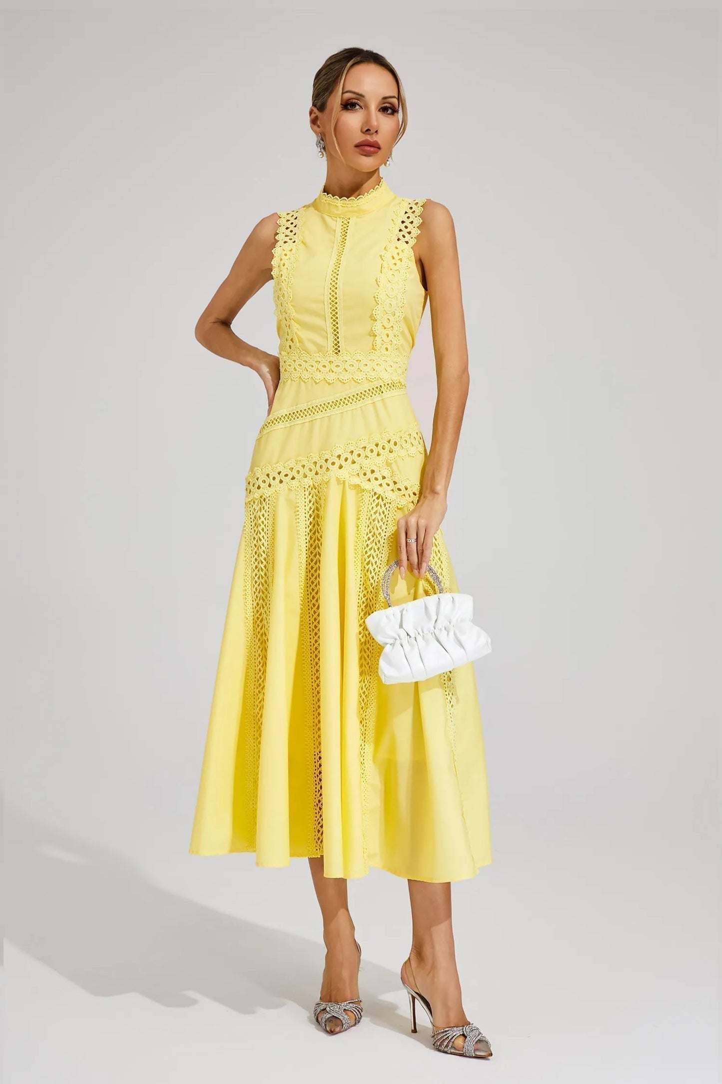 Elegant yellow midi dress with sleeves, showcasing the detailed cutwork and high neck, held with a small white purse.