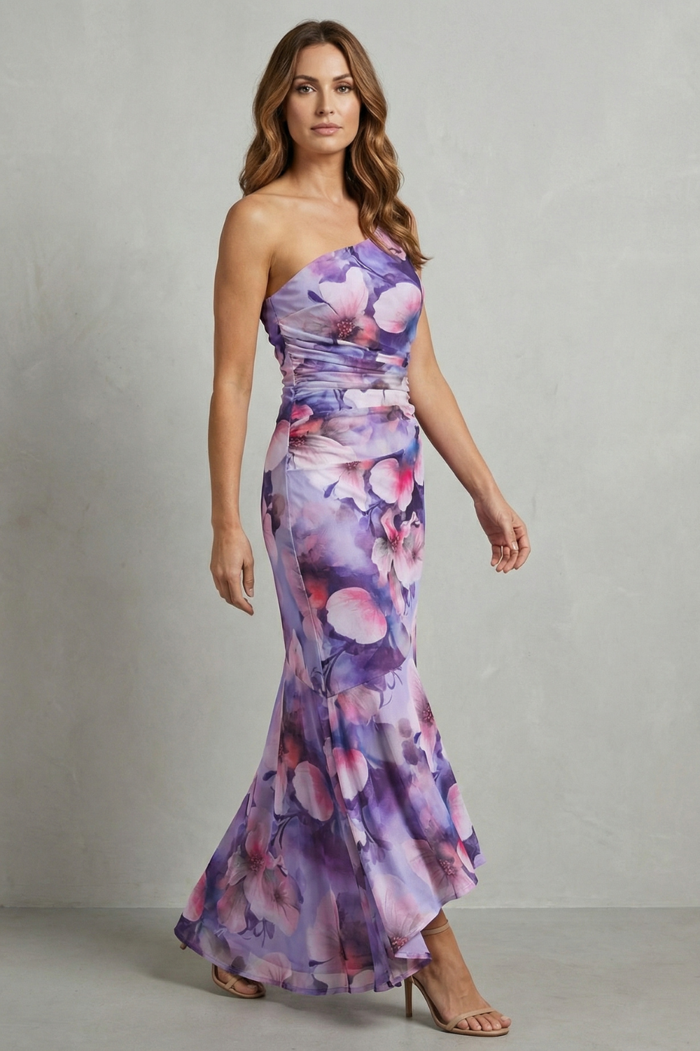 Side profile of a women's wedding guest floral one shoulder maxi dress in purple with pink flowers, showing the high-low hem.