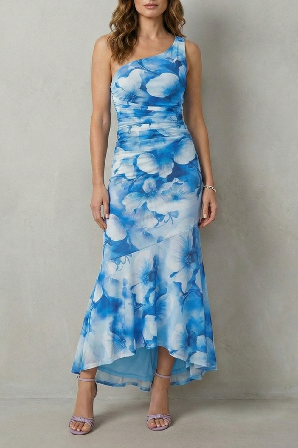Full length view of a women's floral one shoulder maxi dress in blue and white, with a ruched bodice and high-low hem.