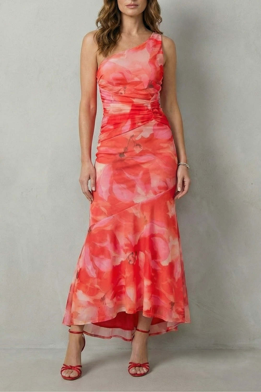 Full length view of a women's floral one shoulder maxi dress in vibrant red and pink, with a ruched bodice and high-low hem.