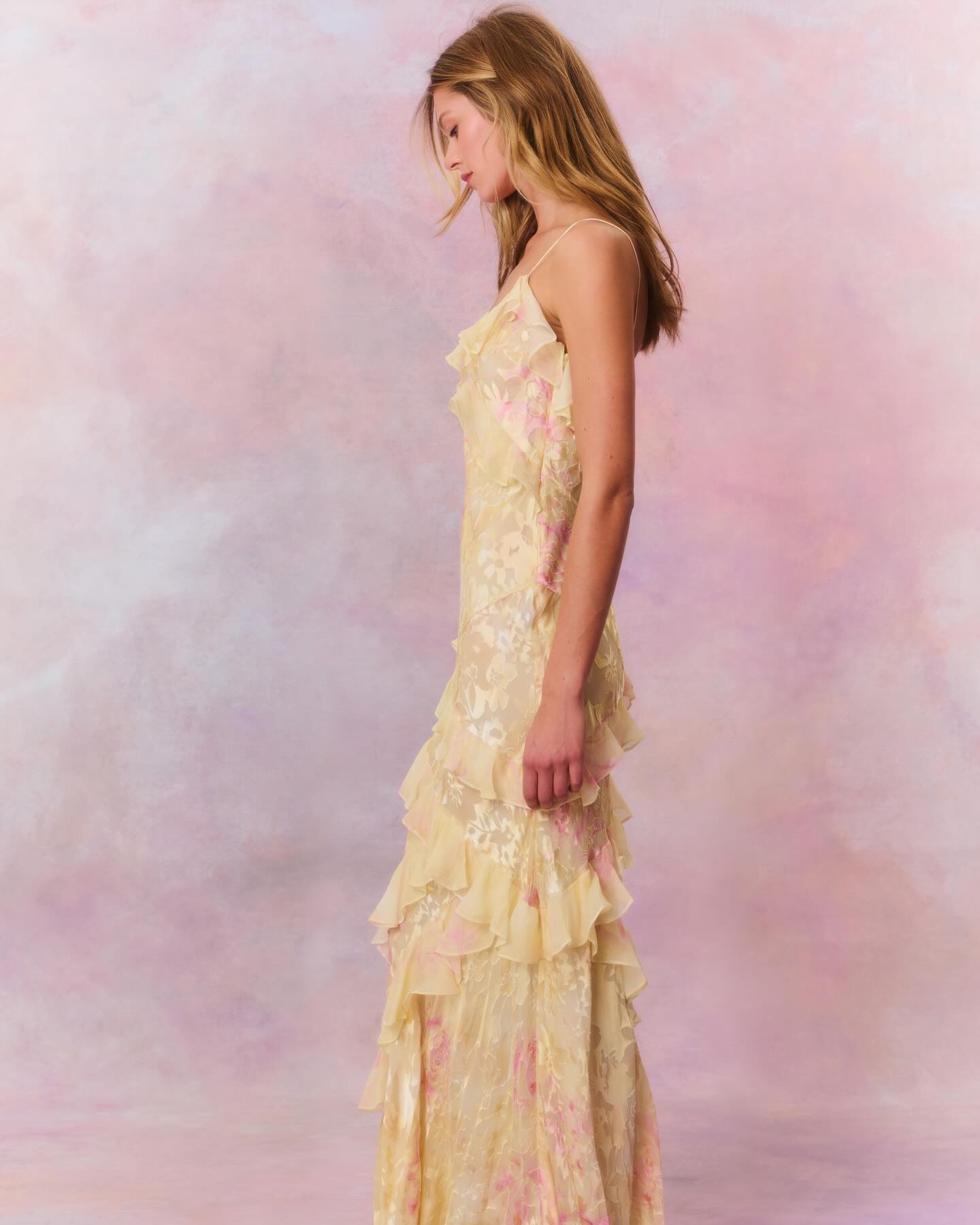 Side view of pale yellow floral slip maxi dress featuring layered ruffles and a flowing hemline