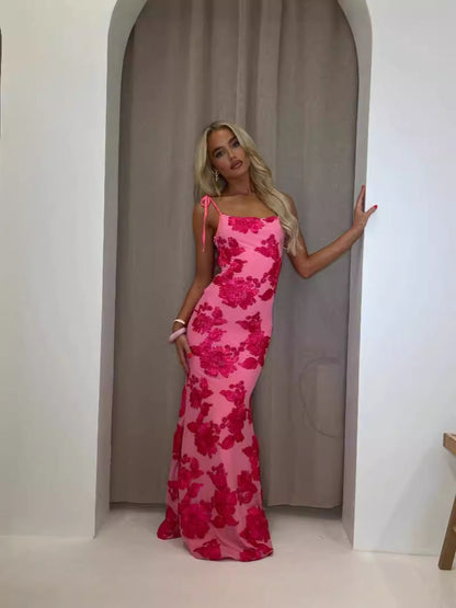 Full length pink floral appliqué maxi dress with tie straps and fitted silhouette, indoor archway scene