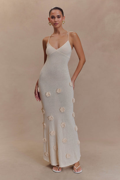 Front view of a cream knit maxi dress with delicate spaghetti straps and scattered 3D floral appliques, perfect for elegant wedding guests.