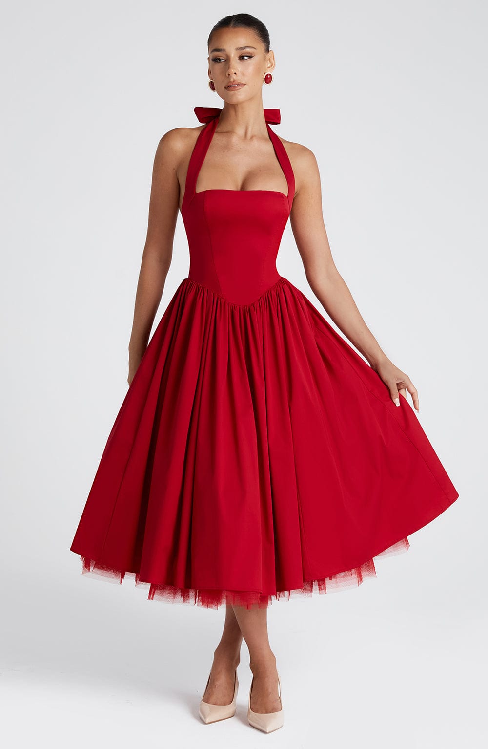 Front view of a women's red halter neck midi dress with a full pleated skirt, subtle tulle hem, and a fitted bodice, ideal for wedding guests.