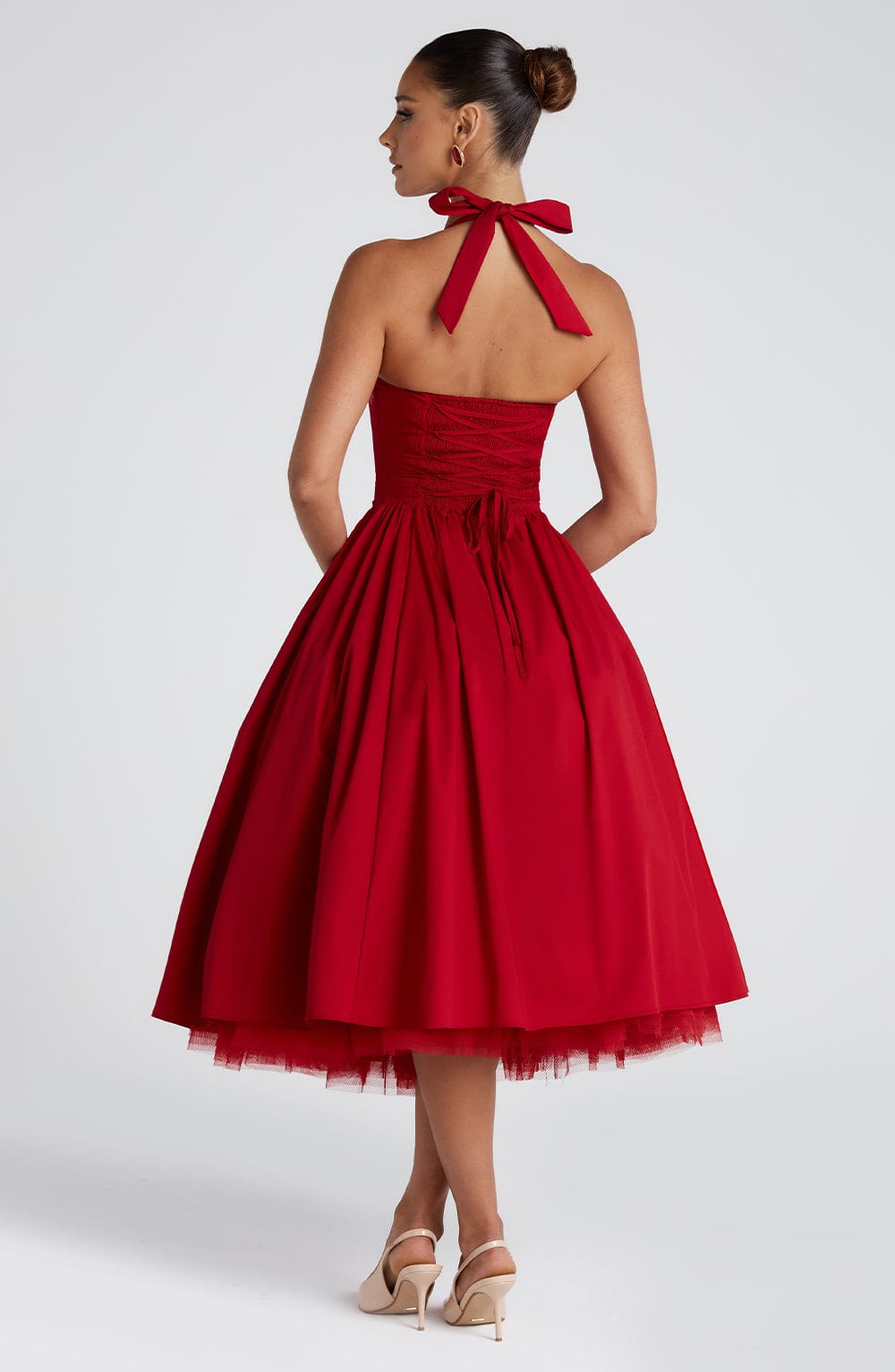 Back view of a red halter neck midi dress, showing the tie-back detail, shirred bodice, and full pleated skirt with a tulle underskirt.