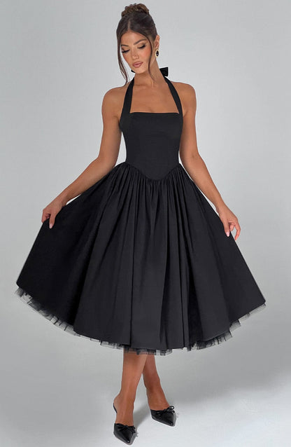 Chic black halter neck midi dress with a full pleated skirt and a visible tulle lining, ideal for vacation outfits or wedding guests.