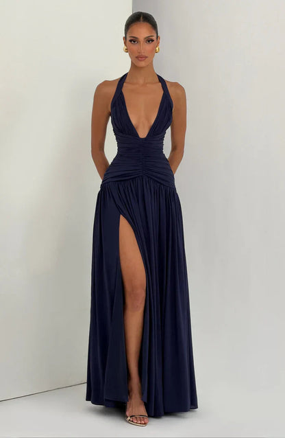 Navy backless halter maxi dress on neutral backdrop, ruched waist and high slit with draped skirt