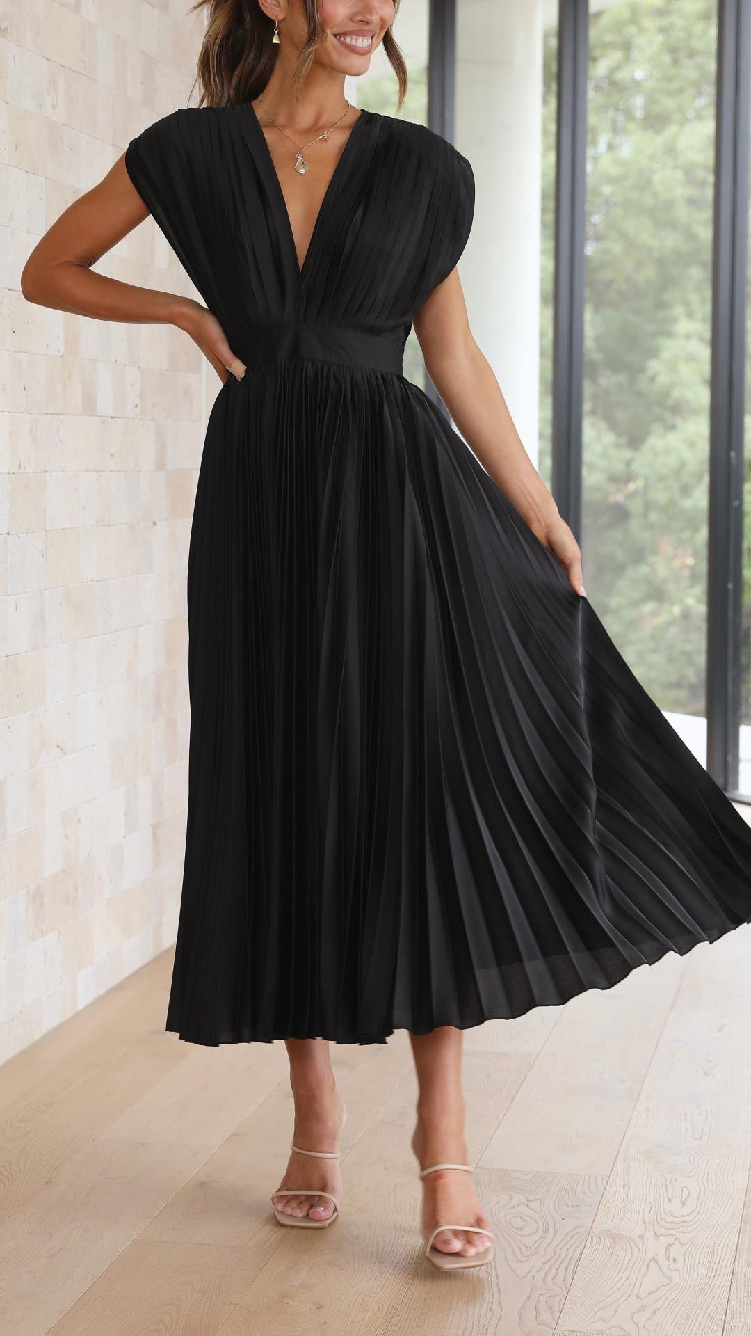 Black pleated v-neck midi dress with cap sleeves, showing movement in the skirt, a graceful wedding guest dress.