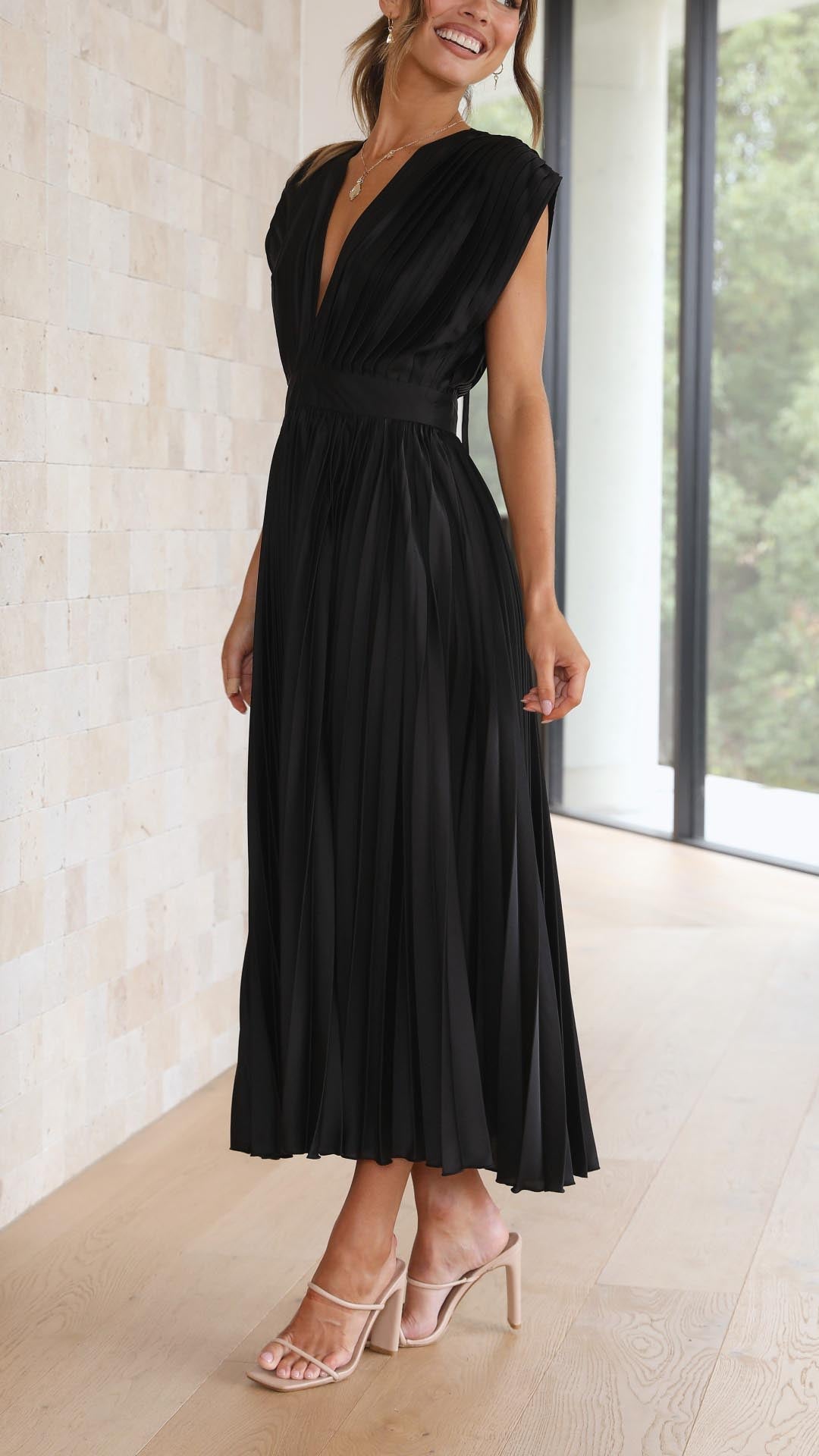 Side view of a black pleated midi dress, highlighting the v-neck and pleated skirt, suitable for wedding guests.