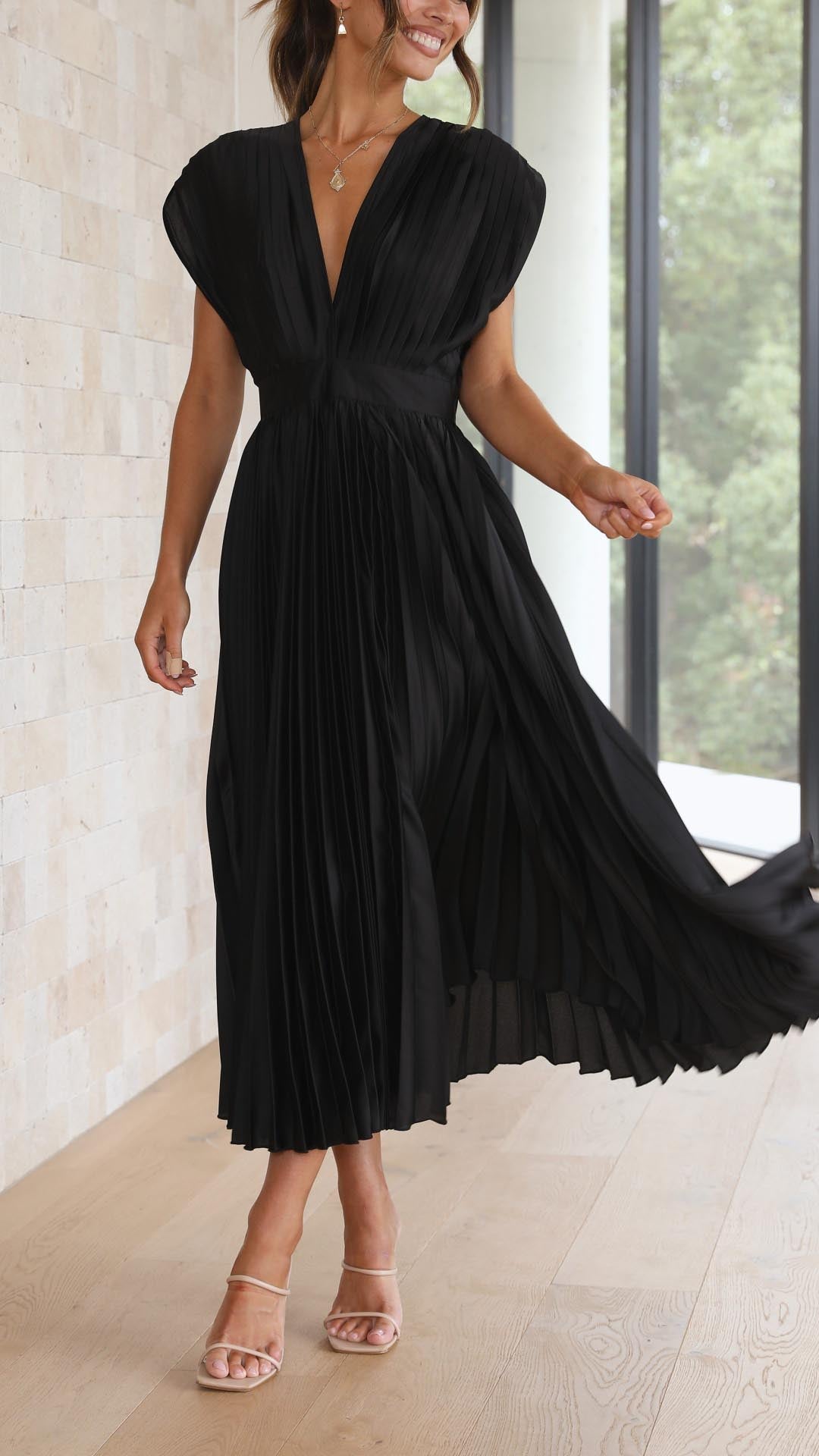 Black pleated v-neck midi dress with cap sleeves, in a dynamic pose, showcasing the flowing pleats, vacation dresses.