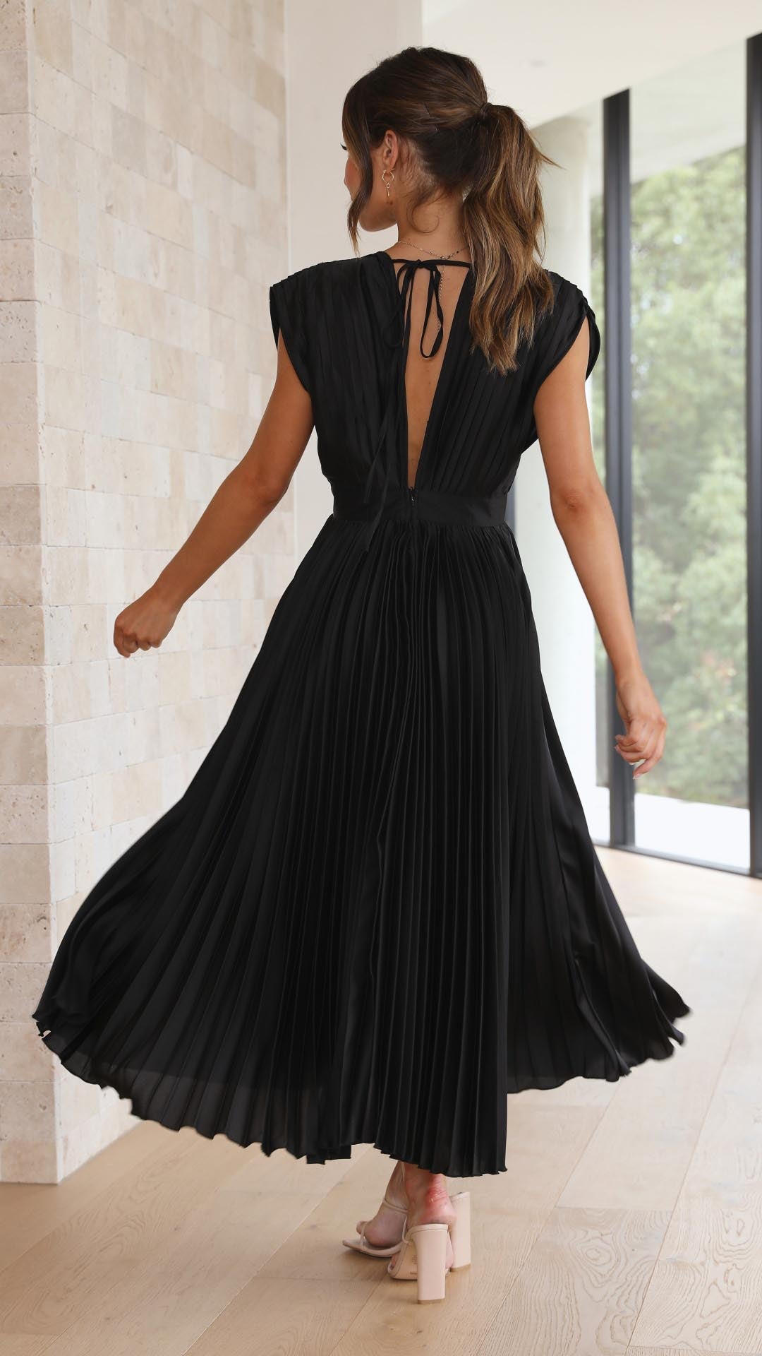 Back view of a black pleated midi dress, with a deep V-back and tie detail, twirling gracefully, womens wedding guest dresses.