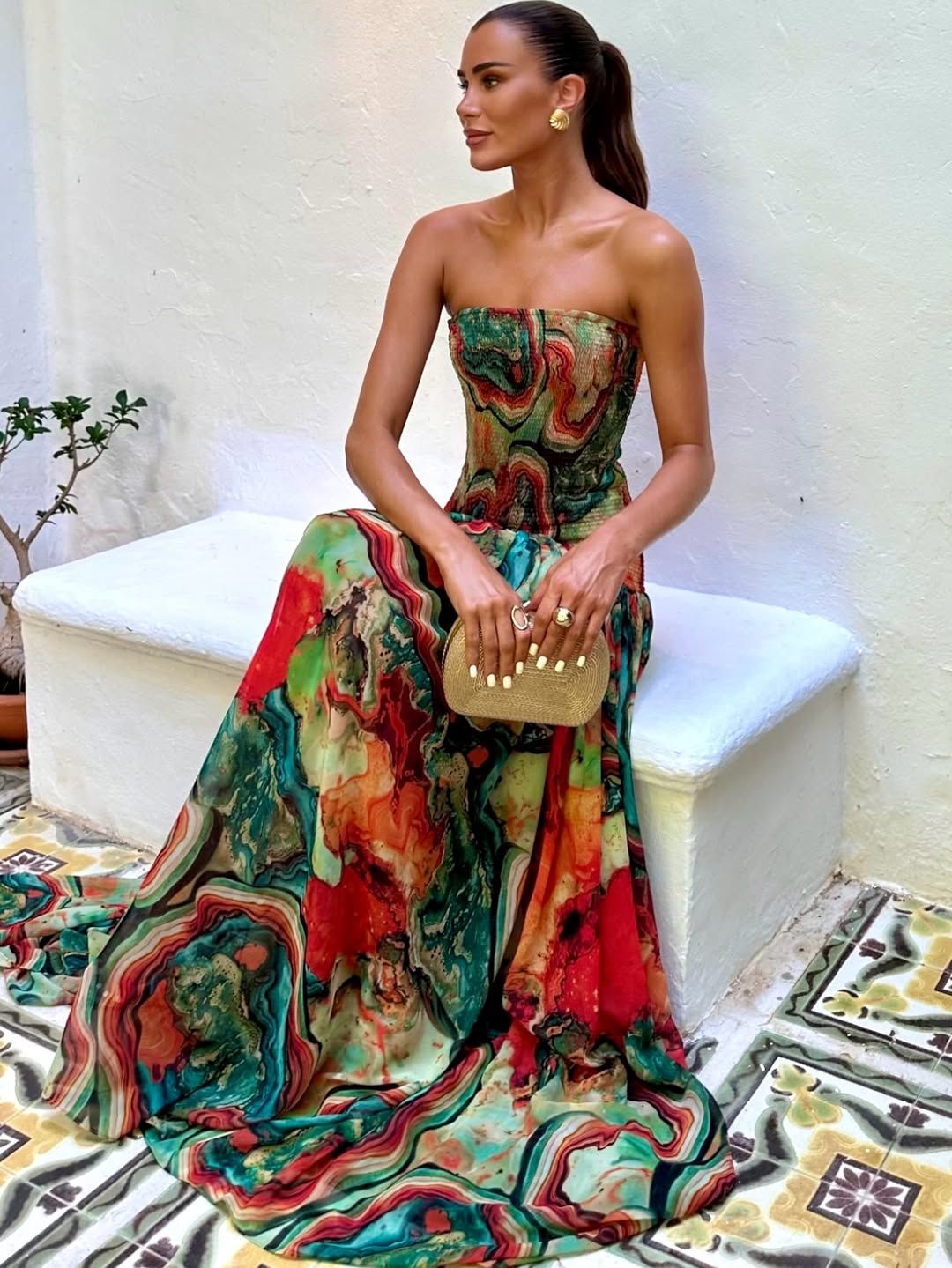 Side view strapless printed maxi dress with fitted bodice and flowing multicolor skirt, clutch in hand