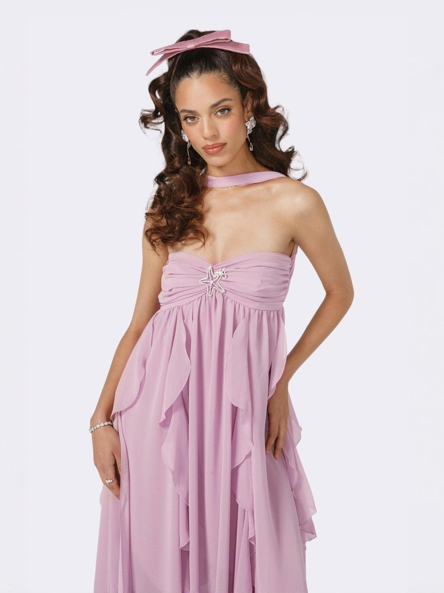 Close-up of the bodice of a light pink strapless maxi dress with an embellished star detail, ruched bust, and ruffled overlay, a stylish wedding guest dress.