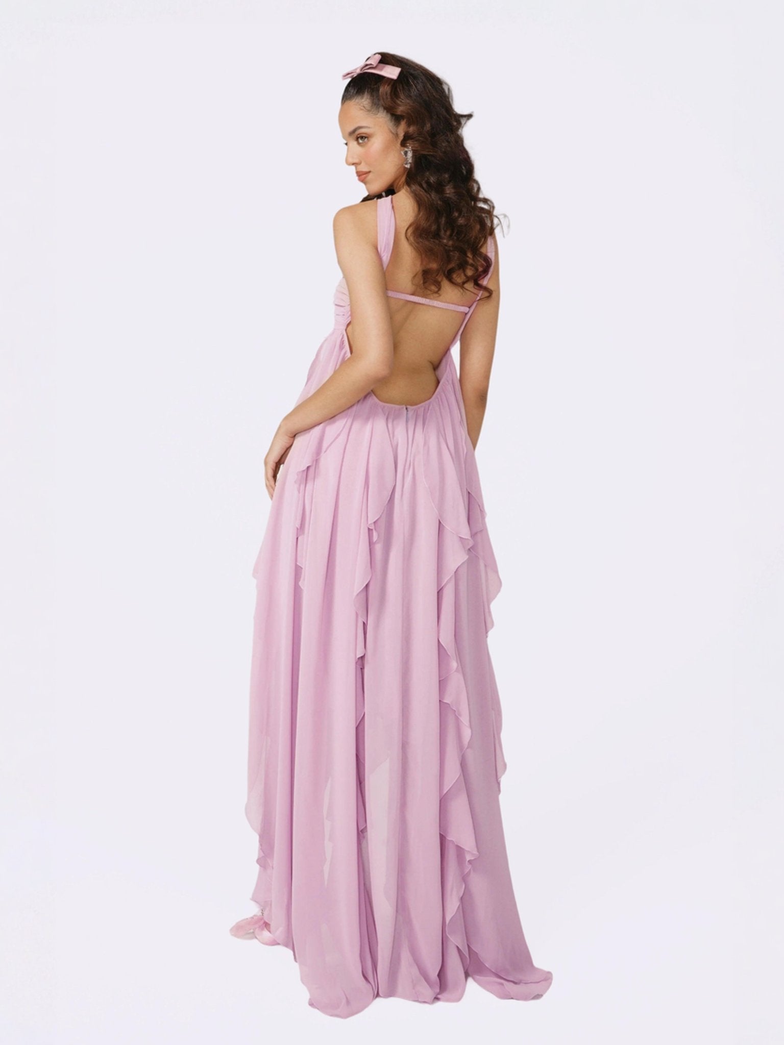 Back view of a woman in a light pink strapless maxi dress, highlighting the open back design and cascading ruffles, a beautiful wedding guest dress.