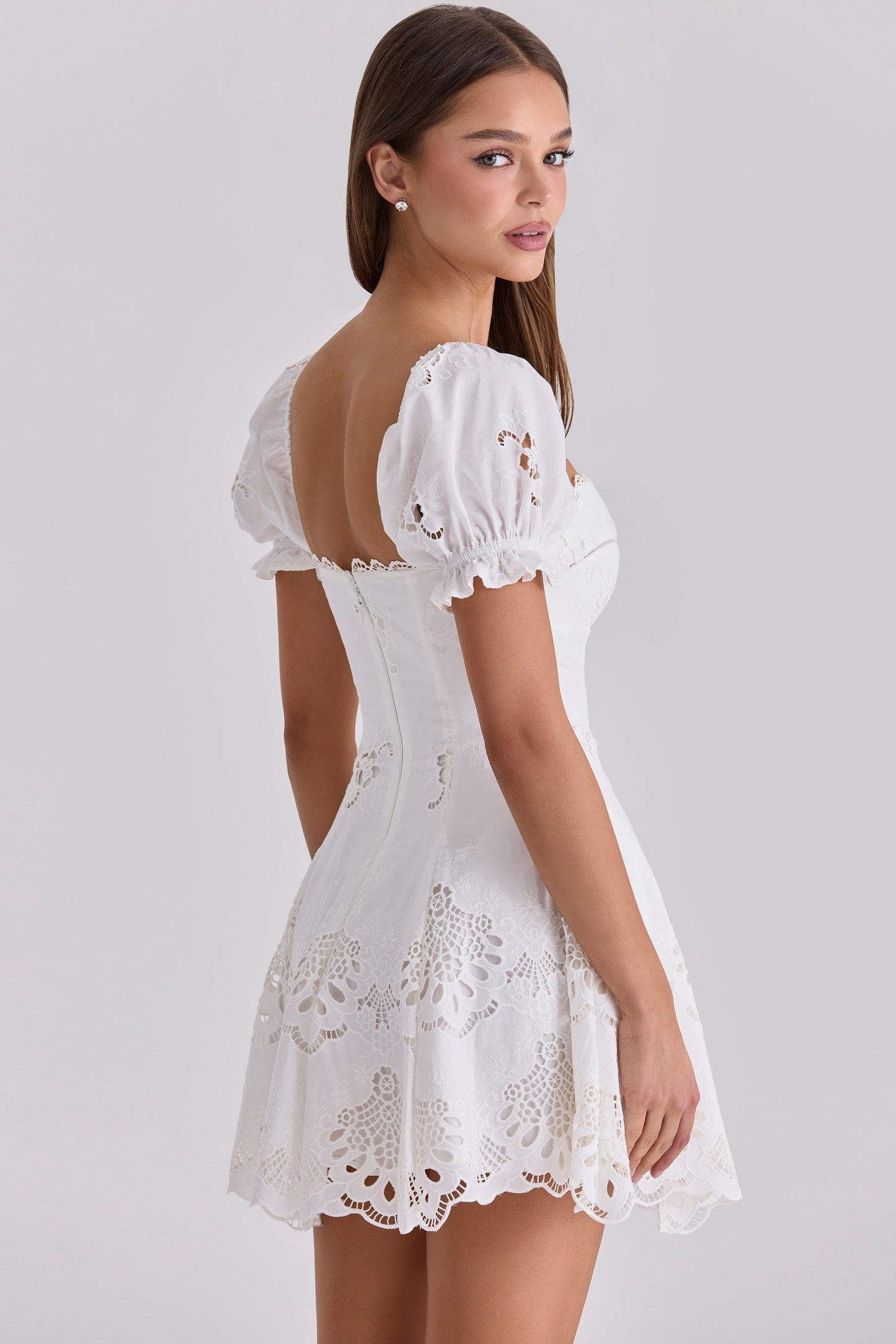 Back three-quarter view of white broderie anglaise mini dress with puff sleeves and lace edging