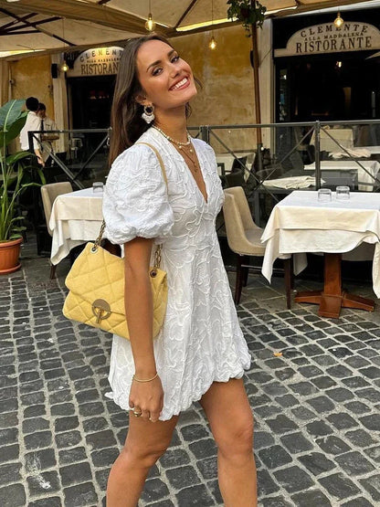 Side view of white floral v-neck puff sleeve mini dress with textured fabric and above-knee skirt