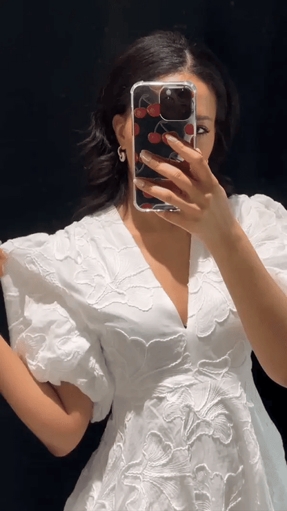Close-up of white floral jacquard mini dress showing deep v-neckline, puff sleeves, and raised embroidery