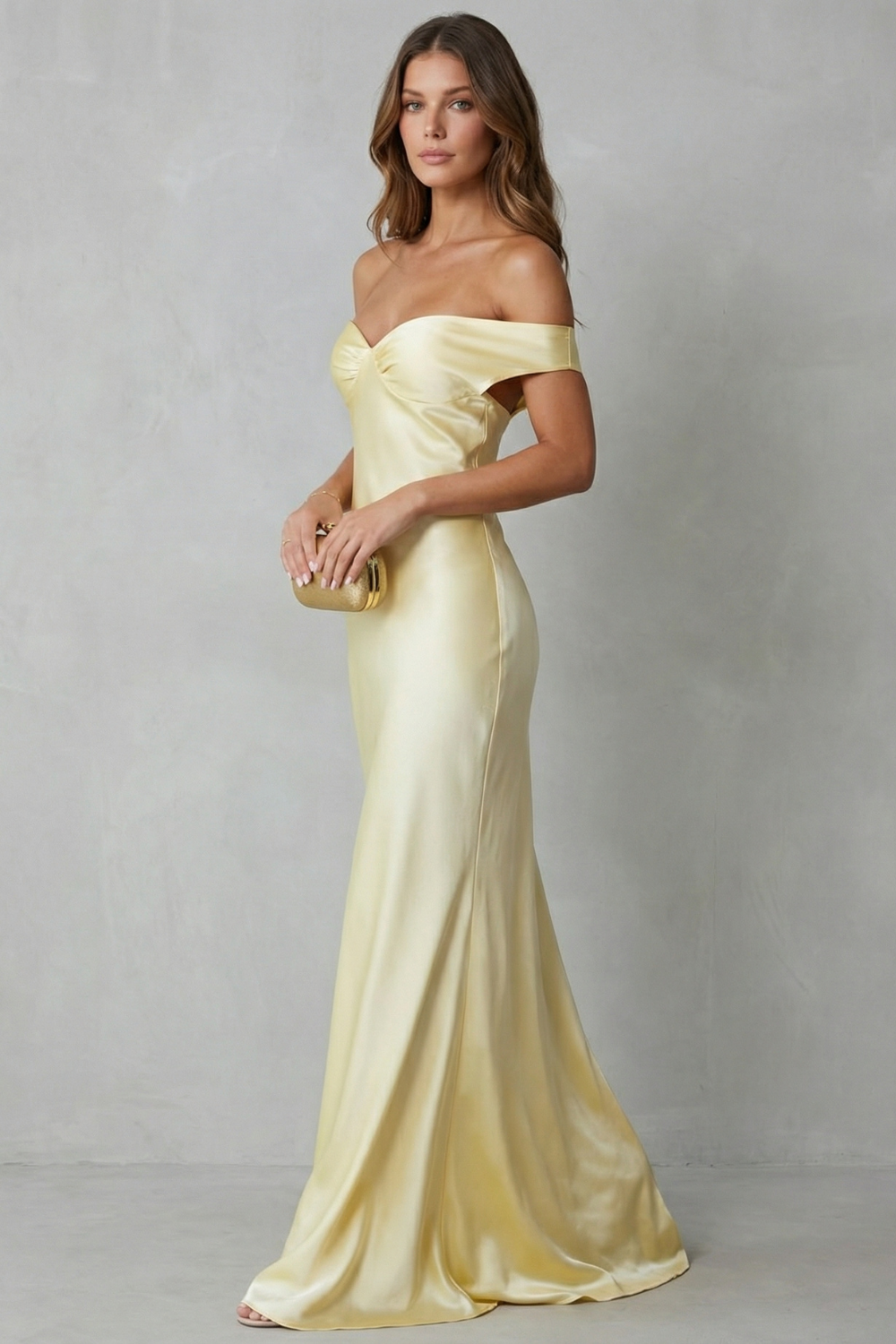 Side profile of a yellow off-shoulder satin maxi dress, showcasing the flowing skirt and fitted bodice.